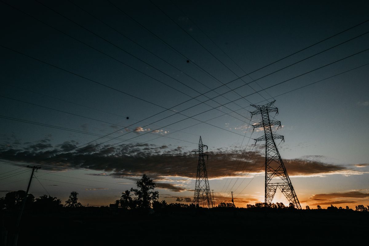 Electricity pylons and power lines silhouetted against a sunset sky